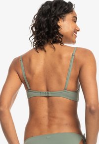 Olijfgroen bikini top met verstelbare bandjes en een haaksluiting aan de achterkant. Gladde textuur, minimalistisch ontwerp en subtiele logo-detail.