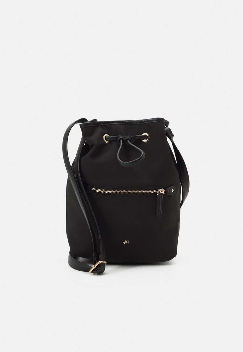 Sac seau noir à cordon avec poche zippée à l'avant, bandoulière réglable et ferrures dorées sur fond uni.