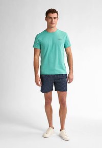 Vaaleanturkoosi puuvillapaita pyöreällä kaula-aukolla, yhdistetty tummansinisiin shortseihin, joissa on valkoinen pilkkukuosi. Valkoiset tennarit täydentävät asun.