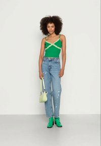 Top verde com detalhes em renda, jeans claros desgastados, botins verdes, e uma pequena bolsa verde-claro. Texturas suaves.