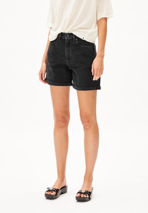 Femme portant un short en denim noir à ourlet roulé, un haut en maille blanc à manches courtes et des sandales à plateforme noires, debout devant un fond blanc.