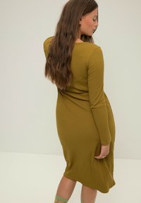 Olivgrünes geripptes Kleid mit langen Ärmeln, tailliertem Design und knielangem Saum. Verfügt über einen leicht drapierten Rücken und eine glatte Textur.