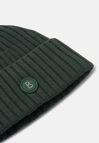 Donkergroene gebreide muts met geribbelde textuur en omgeslagen boord, met een ronde groene knoop met een zilveren "B"-logo.