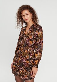 Robe à motifs floraux avec des manches longues, décolleté en V et une ceinture à nouer. Présente des nuances de noir, orange et rose avec une texture de tissu douce.