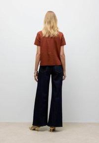 Rust-farvet kortærmet skjorte og brede mørke denim jeans. Jeansene har kontrastsyninger og høj talje. Båret med mønstrede hæle.