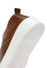 Baskets en cuir marron avec semelle en caoutchouc blanche, dotées d'une semelle intérieure texturée et d'une petite boucle au talon pour un enfilage facile.