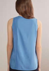 Ärmlös blå topp i slät tyg, med rund halsringning och en avslappnad passform med rundad nederkant, visad bakifrån.