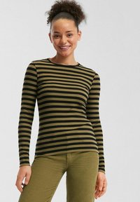 Haut à manches longues de couleur olive avec des rayures horizontales noires. Texture côtelée, col rond, design ajusté. Associé avec un pantalon en velours côtelé olive.