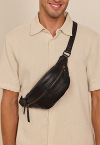 Borsa a tracolla in pelle nera con due tasche con zip, tracolla regolabile e dettagli in metallo color oro. Texture liscia e design elegante.