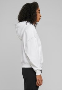 Weiße Kapuzenjacke mit Kordelzug, lockerer Passform, gerippten Bündchen und Saum, getragen über schwarzen Hosen, mit glatter Textur.