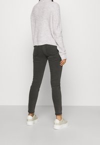 Grijze slim-fit jeans en een lichtgrijze gebreide trui, gecombineerd met witte en beige sneakers, gezien van achteren tegen een effen achtergrond.