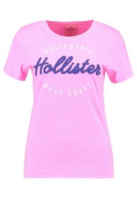 Růžové tričko s krátkým rukávem vyrobené z bavlny. Na přední straně se nachází ve vyvýšeném tmavě modrém písmu nápis "Hollister", s nápisy "California" a "West Coast" tištěnými bíle.