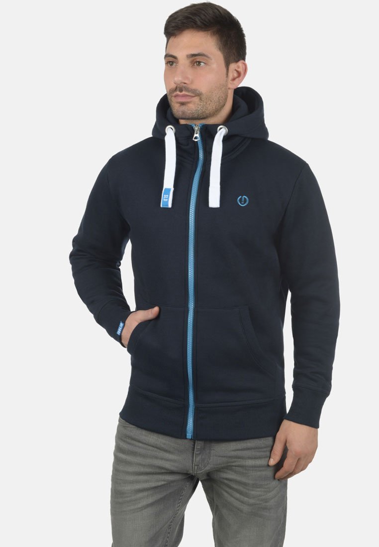 Marineblå zip-up hoodie med høj krave, kontrastblå lynlås og hvide snore. Har frontlommer og et logo på brystet.