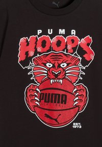 Επιθετ ική κόκκινη τίγρη που κρατά μια κόκκινη баскетбольная μπάλα με την επιγραφή "PUMA", το έντονο "HOOPS" από πάνω και το "EST. 1973" κάτω δεξιά σε μαύρο φόντο.