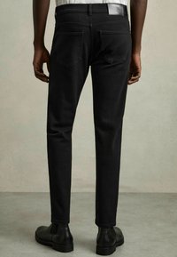 Jeans negre slim-fit cu o textură netedă, având un design clasic cu cinci buzunare, detalii cusute și un patch cu logo pe talie, la spate.