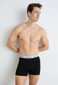 Crne bokserice s bijelim pojasom na kojem piše "BJÖRN BORG", izrađene od mekog, rastezljivog materijala. Uski dizajn s minimalnim šavovima.