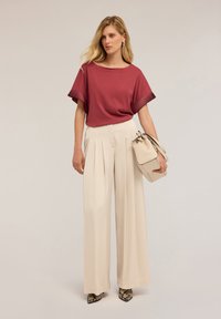 Top corto de manga corta en color marrón burdeos con acentos acanalados; pantalones de pierna ancha en beige claro con plisados; bolso beige; zapatos de tacón alto con estampado de serpiente.