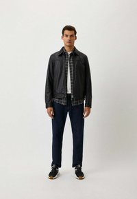 Zwarte leren jas over een geruit shirt, gecombineerd met donkere spijkerbroek en zwarte sneakers. Rechte pasvorm, met een eenvoudige uitstraling en textuur.