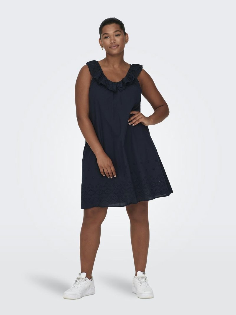 Robe sans manches bleu marine avec un col en volants, un ourlet brodé et une coupe fluide, portée avec des baskets blanches.