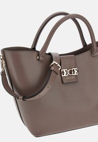 Bolso de mano sintético marrón con asas superiores dobles, correa de hombro ajustable, detalles de herrajes dorados y un cierre decorado con el logotipo.