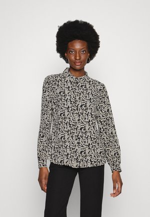 Blusa floral em preto e branco, com mangas longas, colarinho e punhos franzidos, apresentando um tecido leve e texturizado.