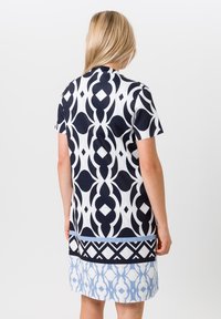 Korte mouwen jurk met een navy en witte patroonontwerp, voorzien van geometrische vormen en banen van blauwe accenten aan de zoom. Glad materiaal.