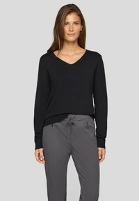 Schwarzer V-Ausschnitt-Pullover mit langen Ärmeln, gerippten Bündchen und Saum; kombiniert mit grauer Hose mit Kordelzug am Bund und Reißverschlusstaschen.