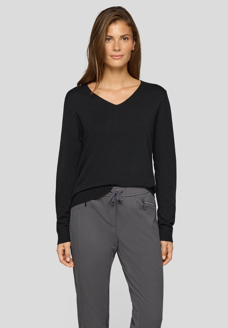 Schwarzer V-Ausschnitt-Pullover mit langen Ärmeln, gerippten Bündchen und Saum; kombiniert mit grauer Hose mit Kordelzug am Bund und Reißverschlusstaschen.