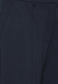 Pantaloni din stofă bleumarin închis cu buzunar lateral vizibil și cusături, evidențiind textura și detaliile de cusut.