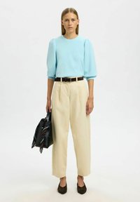 Světle modrá blůza s nafouknutými rukávy, krémové široké kalhoty, hnědý opasek a tmavohnědé boty. Černá kabelka s décor pareo v vzoru.