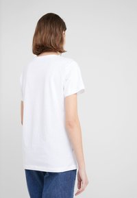 Bílá bavlněná trička s klasickým kulatým výstřihem a krátkými rukávy. Disponuje volným střihem, minimalistickým designem a jemnou texturou.