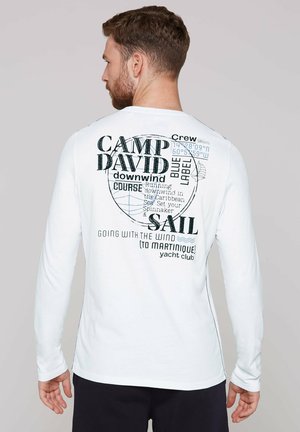 Wit overhemd met lange mouwen en grafische print op de rug met tekst en nautische ontwerpen in zwarte en blauwe accenten. Zachte stoftextuur.