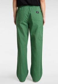 Pantalons larges verts fabriqués dans un tissu texturé, avec des poches arrière et une étiquette sur la taille. Design simple et fonctionnel.