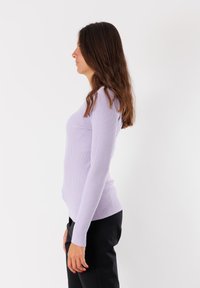 Top lungo a maniche ribatte con una silhouette aderente, scollo rotondo e tessuto texture color lavanda. Abbinato a pantaloni neri.