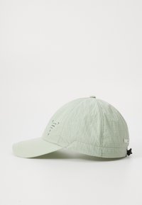 Casquette vert clair en tissu texturé, visière courbée, sangle réglable et détails imprimés subtils à l'avant et sur le côté.