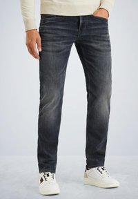 Tamno sivi traperice s ravnim krojem, s laganim izbljeđivanjem i suptilnim stranicama. Nošene s bijelim tenisicama i laganim puloverom.