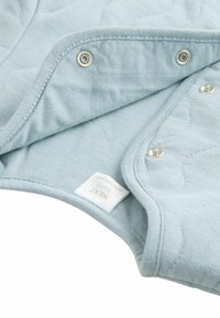 Helle blaue, gestepptes Material mit Druckknopfverschlüssen. Weiche Textur, abgerundete Ränder und ein deutlich sichtbares Etikett mit der Aufschrift "NEXT baby".
