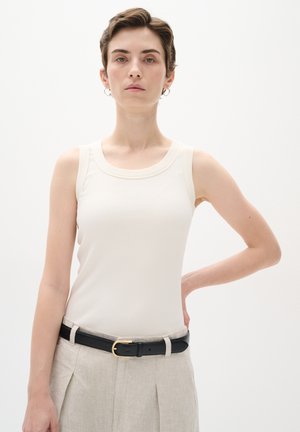 Light beige ribbed tank top with a round neckline, worn with high-waisted light gray trousers and a black belt featuring a gold buckle.