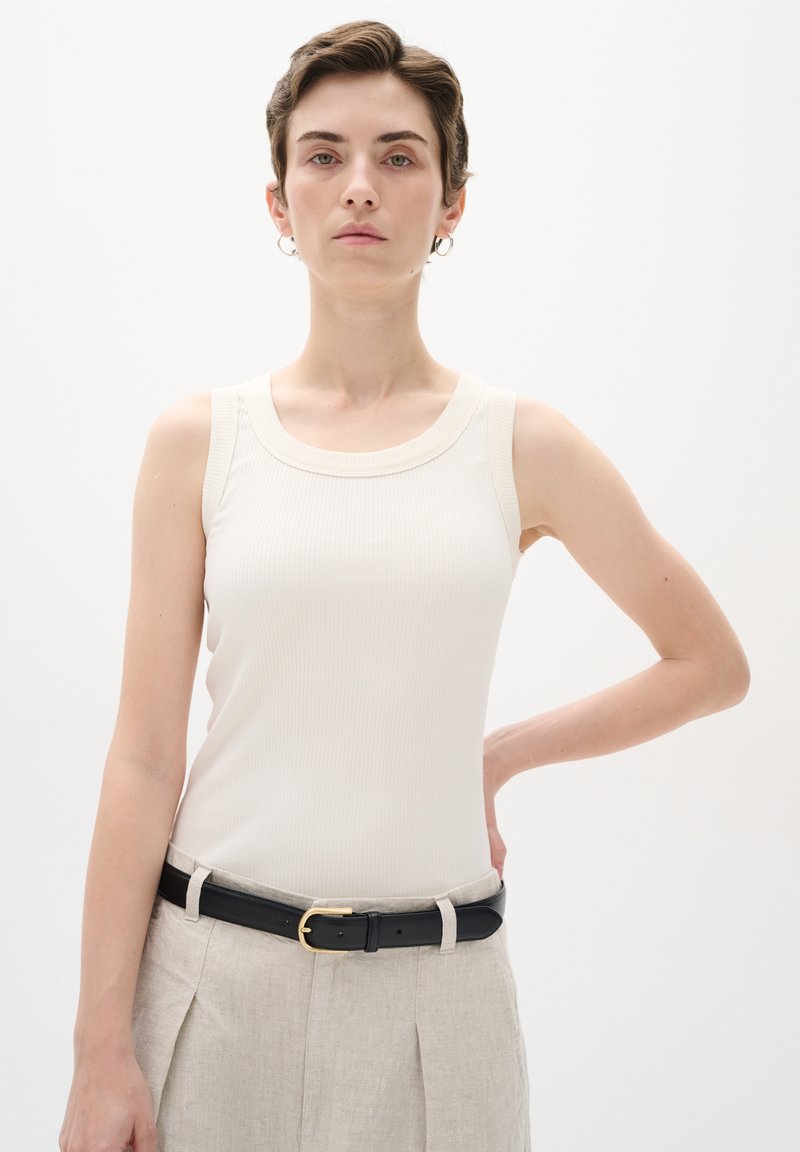 Ljusbeige ribbad tanktop med rund halsringning, kombinerad med högmidjade ljusgrå byxor och ett svart bälte med en guldspänne.