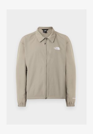 Veste beige The North Face zippée avec col, poignets élastiques et logo sur le côté gauche de la poitrine et la manche droite, présentée sur un fond uni.