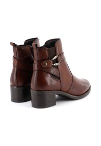 Stivaletti in pelle marrone con punta rotonda, pannelli laterali elastici e fibbie in metallo decorative. Presentano un tacco basso a blocco.