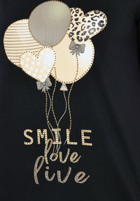 Černá tkanina obsahuje grafiku pěti balónků v hnědých a zlatých odstínech, smíšené vzory a text "SMILE love live" ozdobený kamínky.
