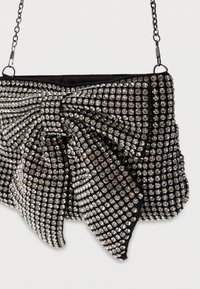 Mała czarna torebka pokryta błyszczącymi cyrkoniami z dużą kokardą z cyrkoniami oraz cienkim metalowym paskiem.