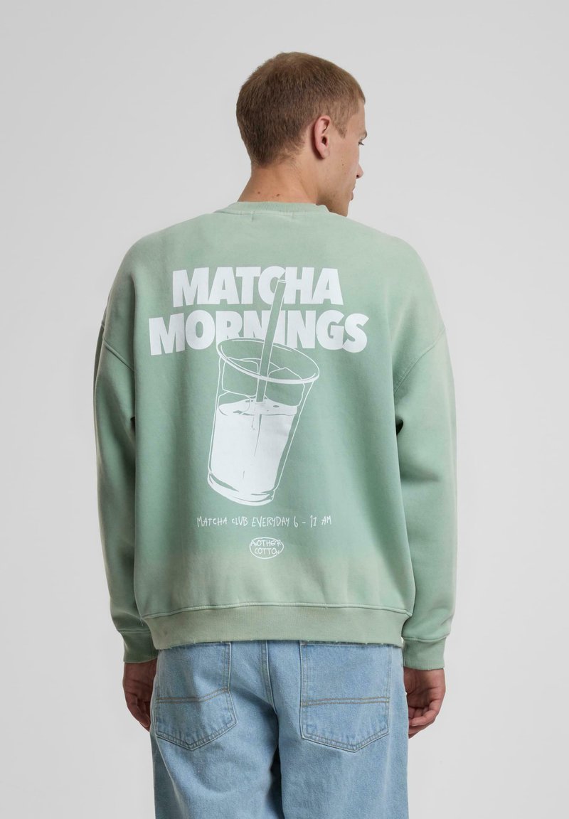 Mintgrønn hettegenser med avslappet passform, som har et stort hvitt grafisk motiv av en drink med teksten "MATCHA MORNINGS" på baksiden.