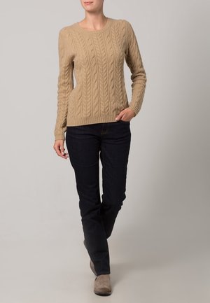 Suéter de punto beige con mangas largas y cuello redondo, combinado con jeans de mezclilla oscura y botas de tobillo gris claro.