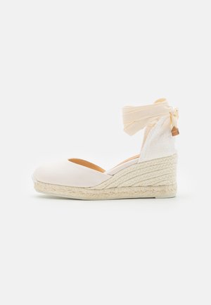 Vinkel espadrille i lys beige stof, med en rund tå, vævet jute platform og et blødt båndankelrem. Tekstureret hæl-accent.