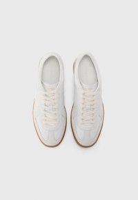 Weiße Leder-Sneaker mit strukturierten Einsätzen, cremefarbenen Schnürsenkeln und einer Gummisohle. Einfaches Design mit sichtbar angebrachtem Logo auf der Zunge.