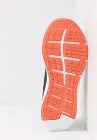 Suela de zapatilla de running Adidas con banda de goma naranja, acentos blancos y texto "ADWEAR" en el talón para tracción y durabilidad.