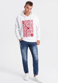 Valkoinen huppari, jossa on punainen "DENIM"-teksti, yhdistettynä sinisiin kuluneisiin farkkuihin ja valkoisiin tennareihin. Hupparissa on nyörikiinnitys ja ribatut hihansuut.