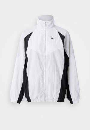 Jachetă Nike din material ușor, albă și neagră. Prezintă guler înalt, închidere cu fermoar, mâneci lungi și un design cu panouri contrastante din țesătură texturată.
